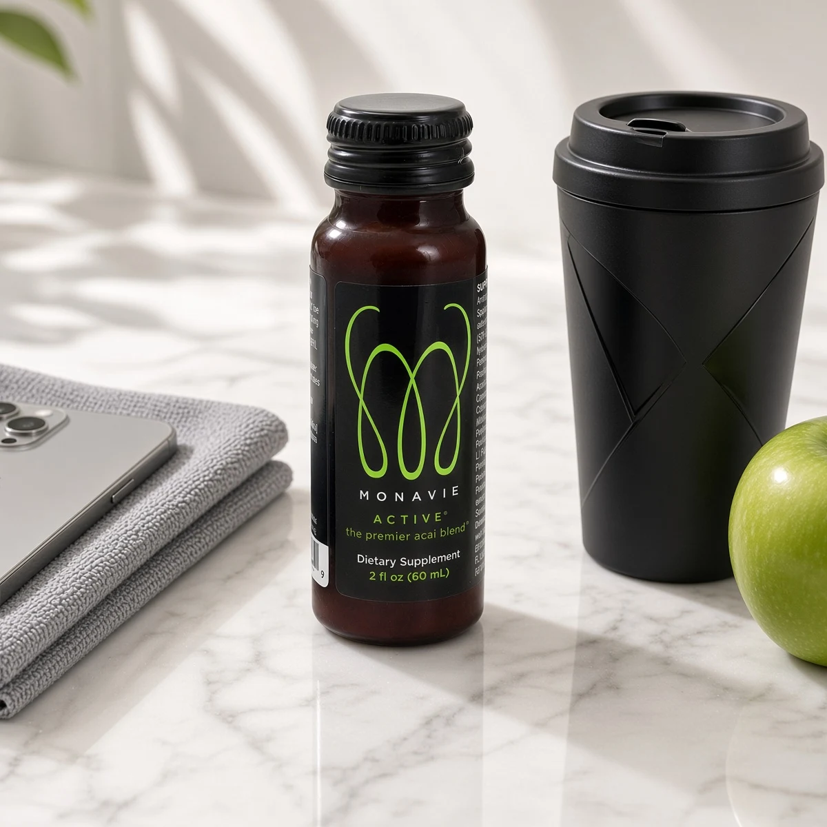 Monavie Active 2 oz bottle beside a coffee cup and an apple